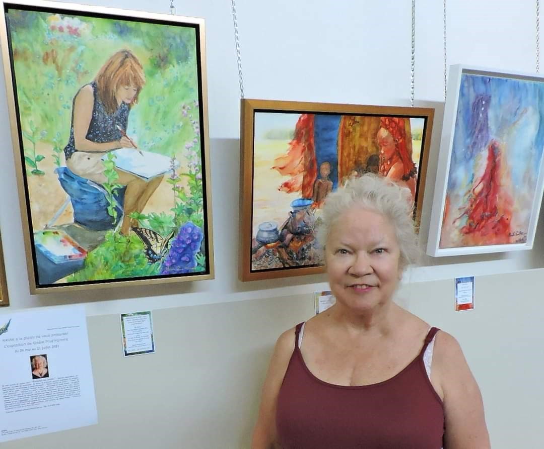 L’artiste Gisèle Prud’Homme posant devant quelques-unes de ses œuvres en expositions dans les couloirs de l’hôpital de Val-des-Sources. 