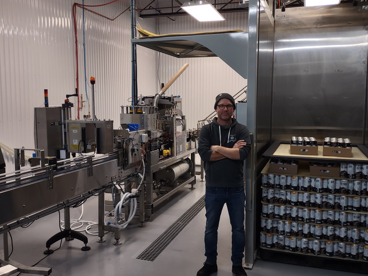 Danick Pellerin copropriétaire de la microbrasserie Moulin 7, posant devant les nouvelles installations d’encannage de l’entreprise, ayant nécessité un demi-million de dollars en investissement.